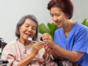 aide assisting the senior woman to toothbrush